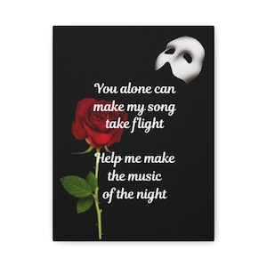May include: A black canvas print featuring a red rose, a white mask, and text from "The Phantom of the Opera." The text reads "You alone can make my song take flight" and "Help me make the music of the night."