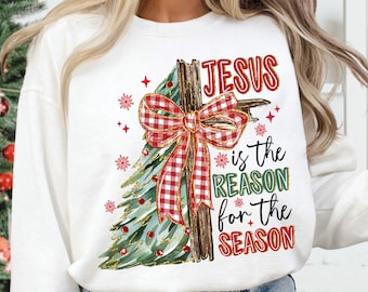 Può includere: Felpa bianca a maniche lunghe con un design ad albero di Natale e la scritta "JESUS is the REASON for the SEASON". L'albero presenta un fiocco a quadri rosso e verde e dettagli rossi e dorati. La felpa è abbinata a jeans blu.