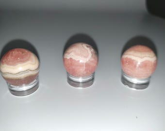 Könnte beinhalten: Drei rosa-weiße, gestreifte Kugeln auf klaren Ständern. Die Kugeln sind aus poliertem Stein.