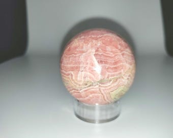 May include: A pink and green sphere of polished gemstone on a clear stand. The sphere has a layered, striated pattern.