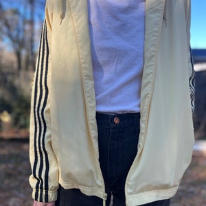 May include: A yellow windbreaker jacket with black stripes on the sleeves. The jacket has a zipper closure and a hood.