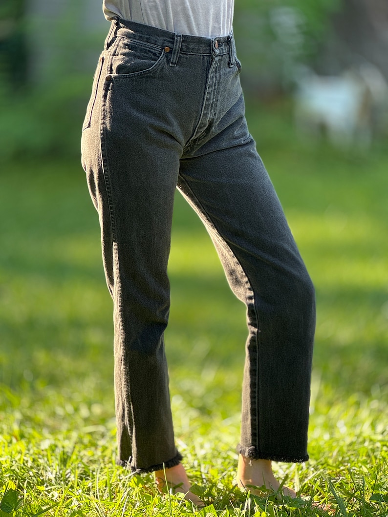 May include: A pair of black denim jeans with a frayed hem. The jeans are fitted through the leg and have a high waist.