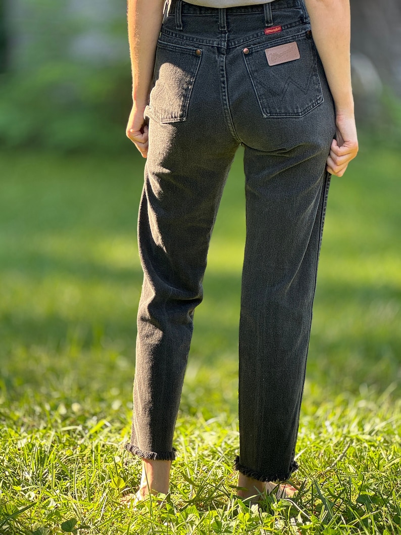 May include: A pair of black denim jeans with a frayed hem. The jeans have a classic five-pocket style and a Wrangler logo on the back pocket.