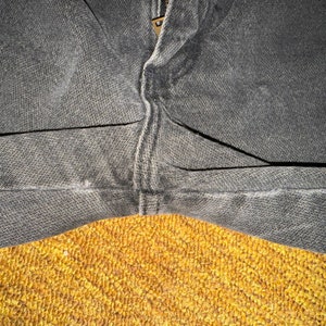 May include: Close-up of a pair of dark gray denim jeans with a seam down the center. The jeans are folded in half and the fabric is textured.