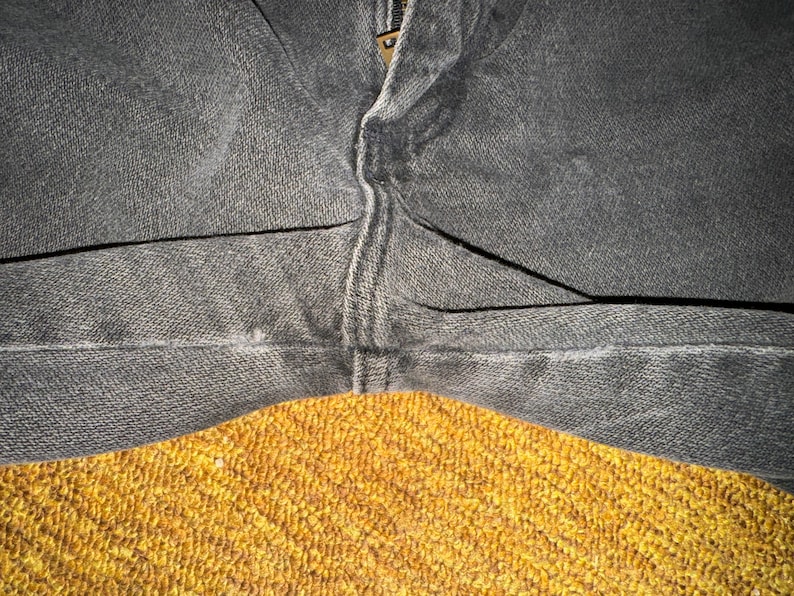 May include: Close-up of a pair of dark gray denim jeans with a seam down the center. The jeans are folded in half and the fabric is textured.