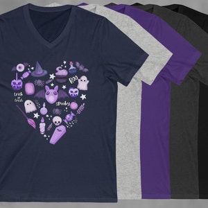 Pu&ograve; includere: Una t-shirt blu navy con scollo a V con un design a forma di cuore viola e bianco che presenta varie icone a tema Halloween, tra cui un fantasma, un pipistrello, un ragno, un cappello da strega, un calderone, una zucca e le parole "Trick or Treat" e "Spooky".