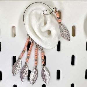 May include: An ear cuff featuring a silver leaf design with pink beads and a silver wire. The ear cuff has multiple dangling leaf charms and is designed to be worn on the ear. The jewelry is displayed on a white background.