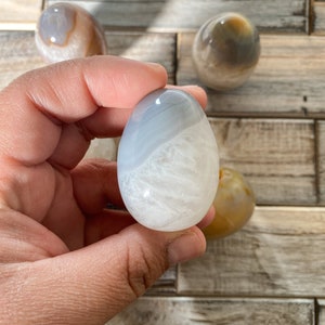 May include: Three polished agate eggs, one white with gray banding, one brown with white banding, and one brown with yellow banding.