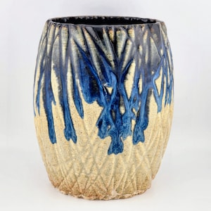 May include: A ceramic planter with a textured, cream-colored exterior and a blue and black glaze. The glaze has a drip effect, creating a unique and artistic design.
