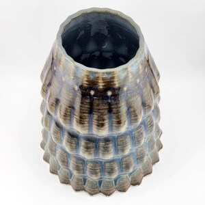 May include: A blue and brown ceramic vase with a textured, layered design. The vase has a wide opening and a rounded bottom.