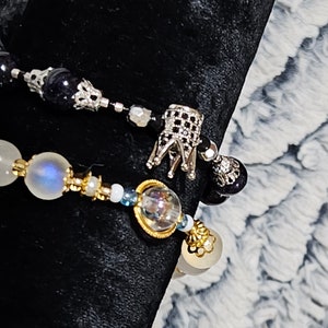 Puede incluir: Dos pulseras con cuentas blancas y azules, una con un dije de corona plateada y la otra con un dije plateado y dorado.