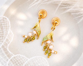 May include: A pair of gold-tone clip-on earrings featuring a green enameled leaf design. Each earring is accented with small white pearls and tiny green beads that hang from the base of the leaf, creating a delicate floral-inspired appearance.