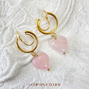May include: A pair of gold clip-on earrings with a delicate swirl design and a dangling pink heart-shaped gemstone.