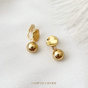 May include: A pair of gold clip-on earrings with a round ball and a textured disc dangling from each clip.