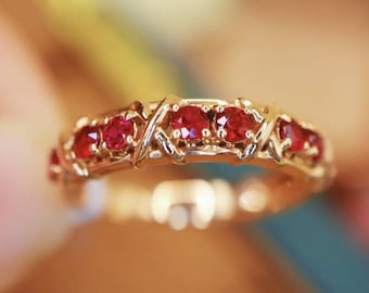 May include: A gold band ring with a criss-cross design and red ruby stones.