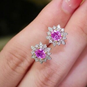May include: A pair of pink sapphire earrings with a diamond halo setting. The earrings are set in white gold and feature a delicate floral design.