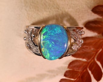 May include: A silver ring with a large oval-shaped opal gemstone set in a gold bezel. The opal is a vibrant blue-green color with flashes of red and yellow. The ring is accented with smaller diamonds.