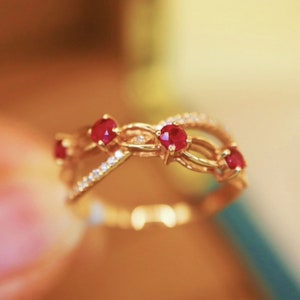 May include: A gold ring with a delicate, interwoven design featuring four red gemstones. The ring is set with small, sparkling diamonds.