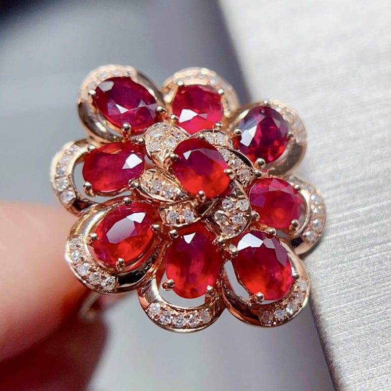 Puede incluir: Anillo de oro con dise&ntilde;o floral, engastado con rub&iacute;es ovalados y peque&ntilde;os diamantes. Los rub&iacute;es forman los p&eacute;talos, mientras que los diamantes a&ntilde;aden brillo. Una joya llamativa para ocasiones especiales.