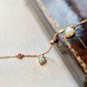 Puede incluir: Un delicado collar de cadena de oro con tres colgantes: una pequeña piedra preciosa rosa, una piedra preciosa de ópalo más grande en un engaste en forma de corazón y una piedra preciosa de ópalo más pequeña.