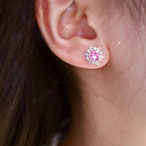 May include: A pair of earrings with a pink gemstone surrounded by smaller clear gemstones in a flower-shaped setting.