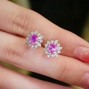 May include: A pair of pink sapphire earrings with a floral design. The earrings are set in white gold and feature a cluster of small diamonds surrounding the center stone.