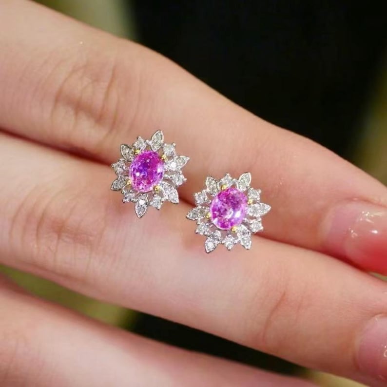 May include: A pair of pink sapphire earrings with a floral design. The earrings are set in white gold and feature a cluster of small diamonds surrounding the center stone.