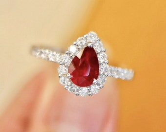 Puede incluir: Un anillo de plata con un rubí en forma de pera y un halo de diamantes más pequeños.
