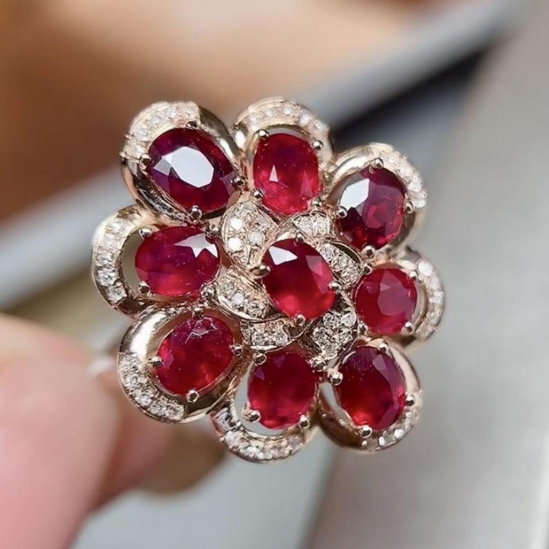 Puede incluir: Un anillo con forma de flor con rub&iacute;es rojos intensos de corte ovalado. Los p&eacute;talos del anillo est&aacute;n formados por los rub&iacute;es, con peque&ntilde;os diamantes que acent&uacute;an los bordes. El engaste es de un tono oro rosa c&aacute;lido, creando una joya lujosa y llamativa.