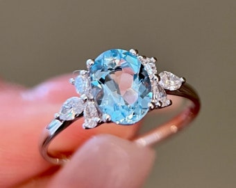 May include: A silver ring with a light blue oval gemstone surrounded by smaller clear gemstones.