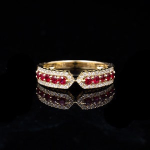 May include: A gold band ring with a V-shaped opening, set with red rubies and clear diamonds.