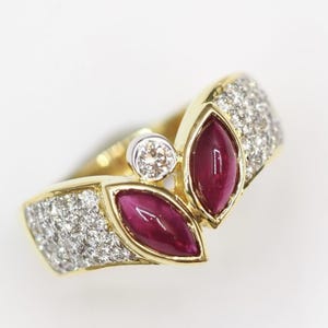 Puede incluir: Un anillo de oro con dos piedras de rubí rojo y un solo diamante. El anillo está engastado con diamantes pavé.
