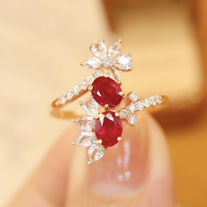 May include: A gold ring with two red ruby gemstones and a diamond flower design.