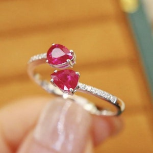 May include: A silver ring with two pear-shaped ruby gemstones and a band of small diamonds.