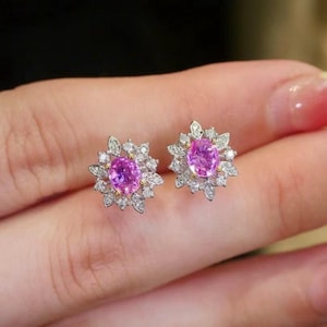 May include: A pair of pink sapphire earrings with a diamond halo setting. The earrings are set in white gold and have a floral design.
