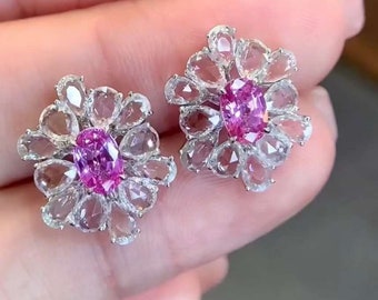 Può includere: Un paio di orecchini d'argento con pietre preziose rosa incastonate in un design floreale. Gli orecchini sono realizzati con piccole pietre preziose trasparenti che circondano una pietra preziosa rosa più grande al centro.