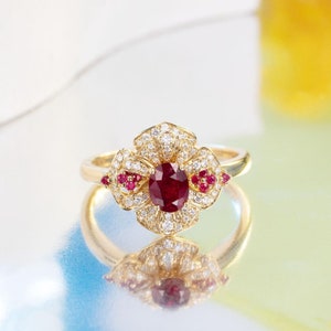 Puede incluir: Un anillo de oro con un gran rub&iacute; ovalado rodeado de diamantes m&aacute;s peque&ntilde;os. El anillo est&aacute; engastado en un dise&ntilde;o con forma de flor con rub&iacute;es m&aacute;s peque&ntilde;os a los lados.