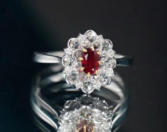 Op de afbeelding: Een zilveren ring met een grote ovale robijn omringd door een halo van kleinere diamanten.