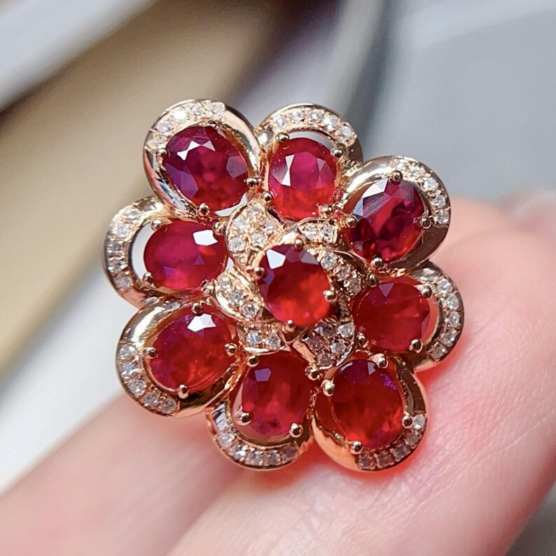 Puede incluir: Anillo de oro con forma de flor, engastado con rub&iacute;es de corte ovalado y peque&ntilde;os diamantes. El dise&ntilde;o presenta un grupo central de rub&iacute;es, rodeado de p&eacute;talos de rub&iacute;, con detalles de diamantes. Una joya.