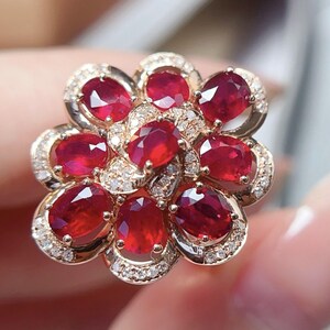 Puede incluir: Un anillo con forma floral, con piedras rojas ovaladas, probablemente rub&iacute;es, engastadas en metal dorado. El anillo est&aacute; adornado con peque&ntilde;as piedras transparentes, posiblemente diamantes, creando un efecto brillante y elegante.