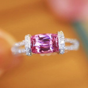 May include: A pink gemstone ring with a rectangular cut stone set in a silver band with small diamonds on the sides.