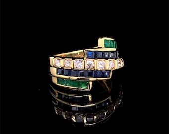 Può includere: Un anello d'oro con un design multistrato. L'anello presenta file alternate di diamanti, zaffiri e smeraldi. Le pietre preziose sono incastonate in uno stile a canale, creando un look audace e lussuoso. L'anello è esposto su sfondo nero.