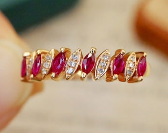 May include: A gold band ring with a row of alternating marquise-shaped ruby and diamond stones.