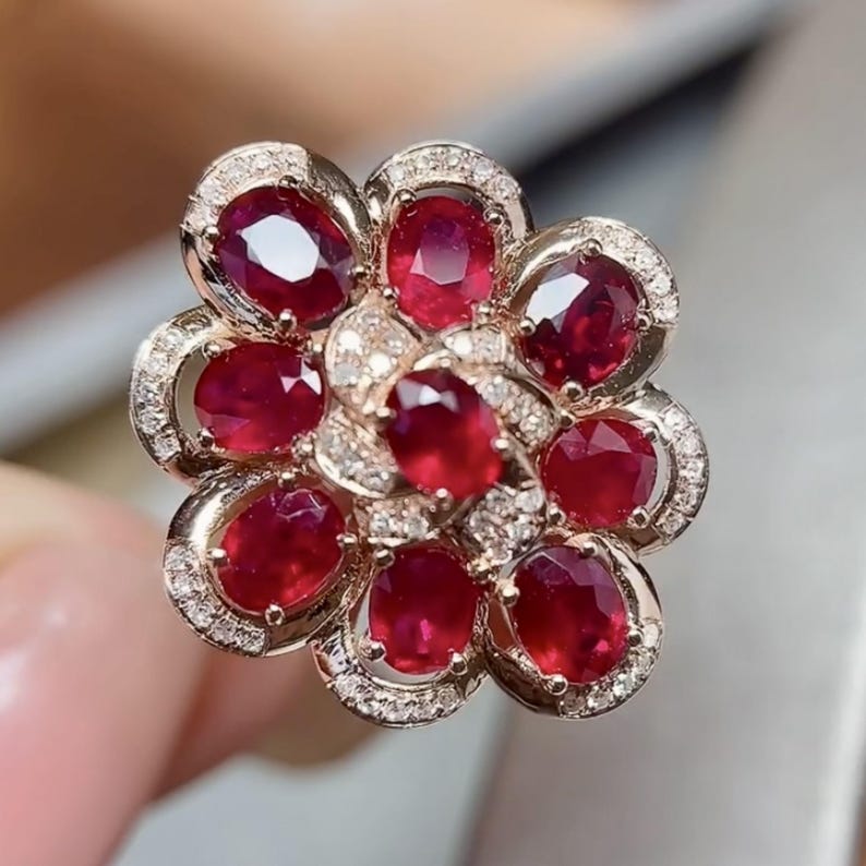 Puede incluir: Un anillo con forma de flor con rub&iacute;es de corte ovalado y peque&ntilde;os diamantes. El anillo tiene una banda dorada y un dise&ntilde;o floral, con los rub&iacute;es dispuestos para parecer p&eacute;talos. Los diamantes est&aacute;n engastados alrededor de los rub&iacute;es.