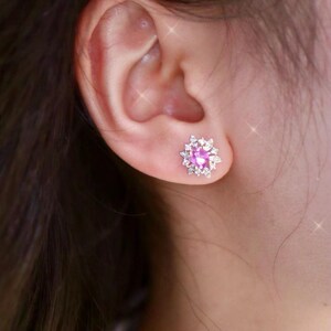 May include: A pair of pink gemstone earrings with a cluster of smaller white gemstones surrounding the center stone.