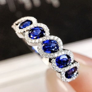 May include: A silver band ring with five oval-shaped blue sapphires set in a halo of smaller diamonds.