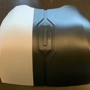Puede incluir: Una pieza de pecho impresa en 3D para cosplay o la fabricaci&oacute;n de disfraces. La pieza est&aacute; hecha de dos mitades, una blanca y una negra, y presenta un dise&ntilde;o geom&eacute;trico.