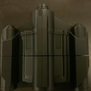 May include: A black plastic model of a spaceship with a long, narrow body and two side wings. The model has a detailed design with multiple sections and a pointed nose.