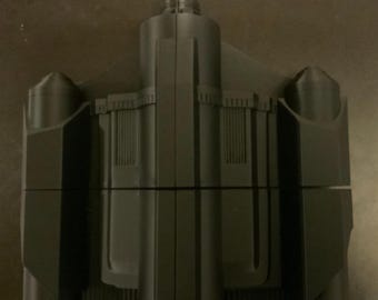 May include: A black plastic model of a spaceship with a long, narrow body and two side wings. The model has a detailed design with multiple sections and a pointed nose.