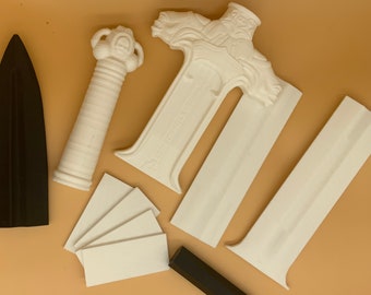 Puede incluir: Un conjunto de piezas de plástico blanco para ensamblar una espada, que incluye un mango, una hoja y una guarda. Las piezas están dispuestas sobre una superficie marrón. También hay una hoja de plástico negro y un juego de espaciadores de plástico blanco.